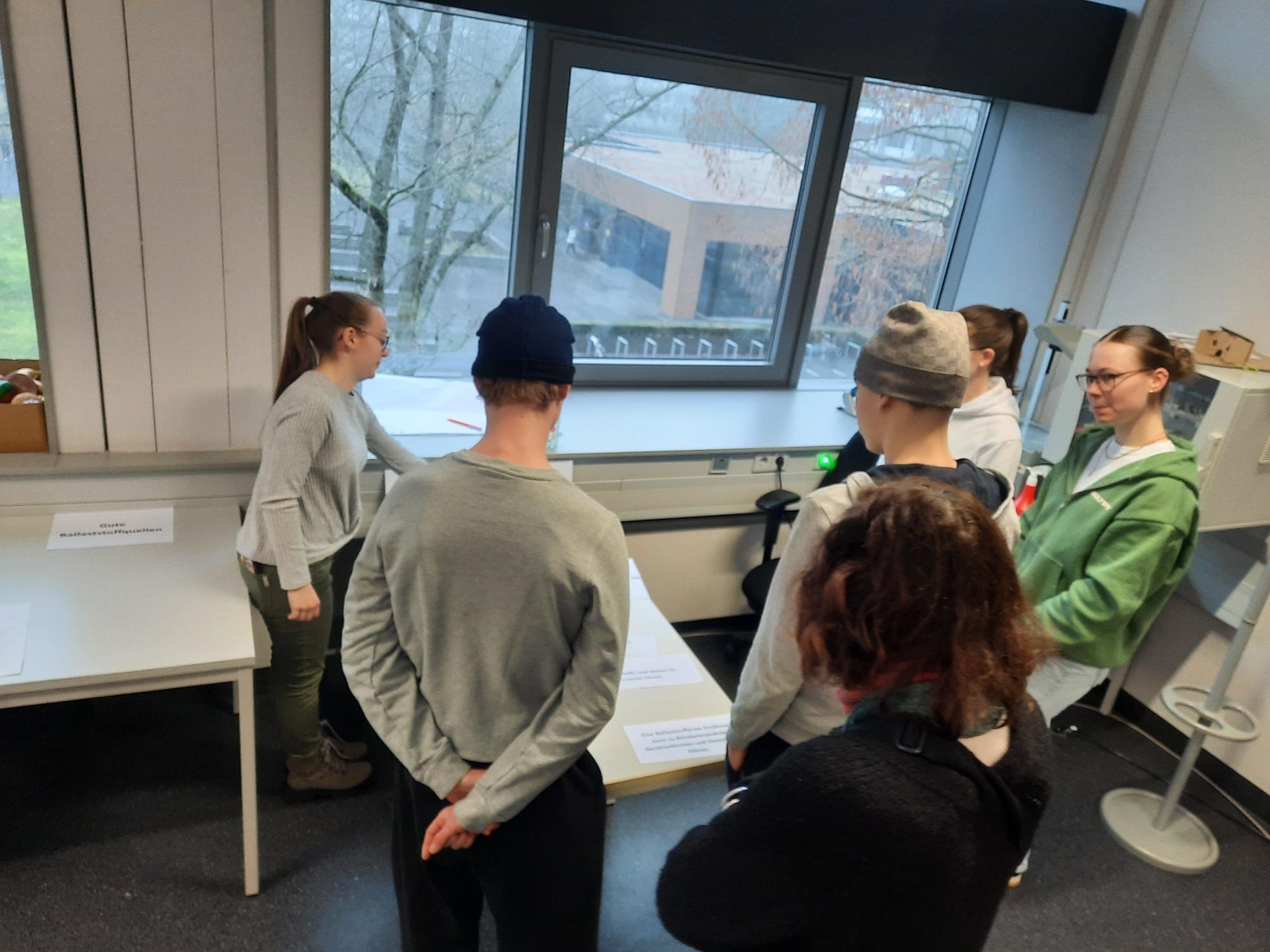 Eine Gruppe von Menschen steht in einem Raum und schaut aus einem Fenster.