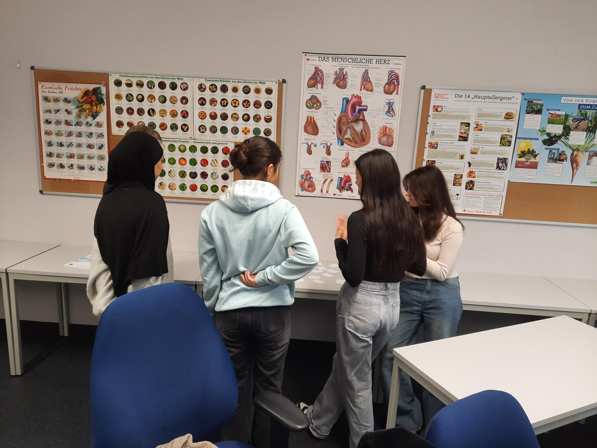 Vier Personen stehen vor einer Tafel mit Ernährungsinformationen in einem Klassenzimmer.