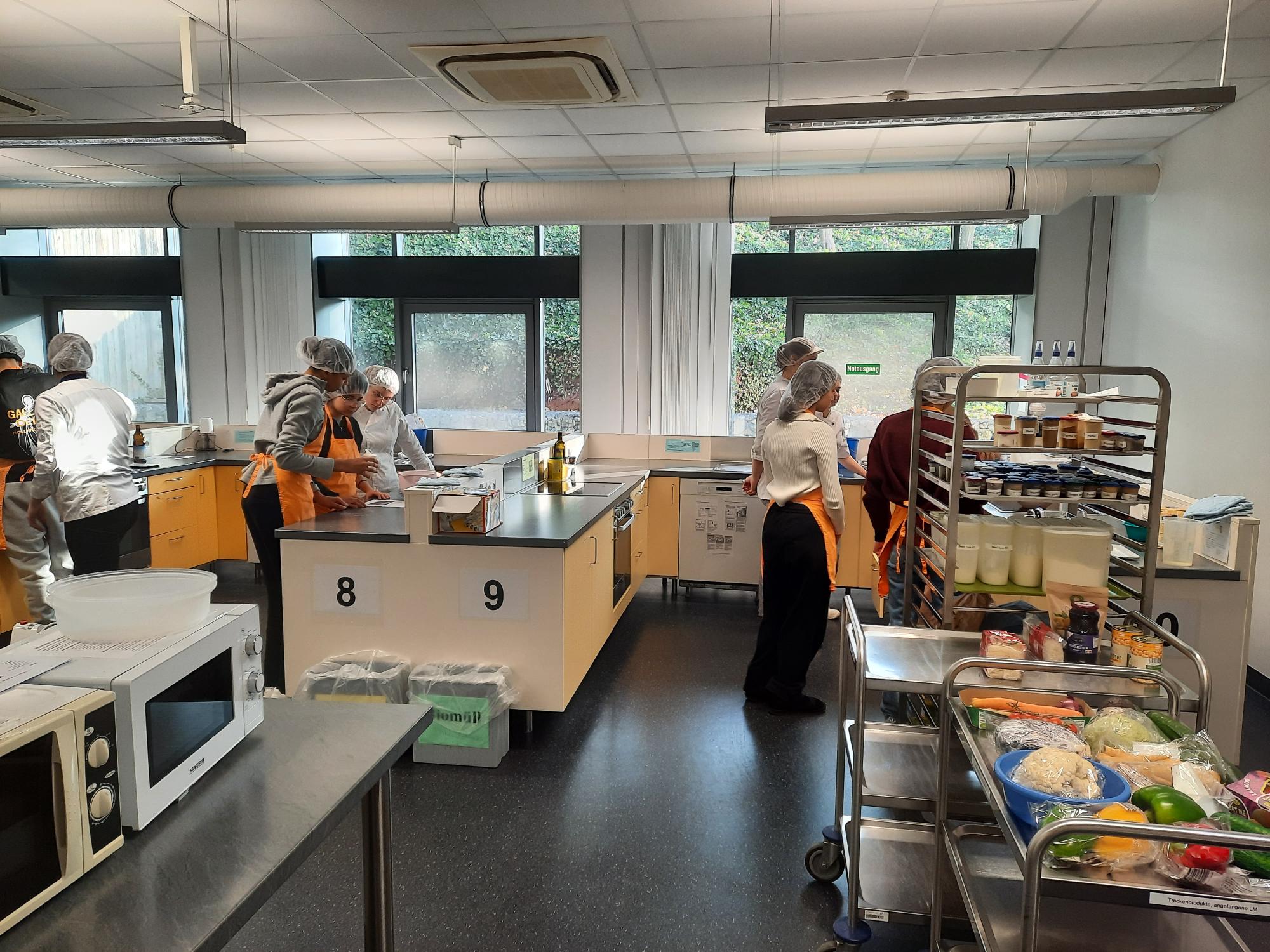 Eine Gruppe von Menschen kocht in einer großen Küche mit Arbeitsstationen und Zutaten.