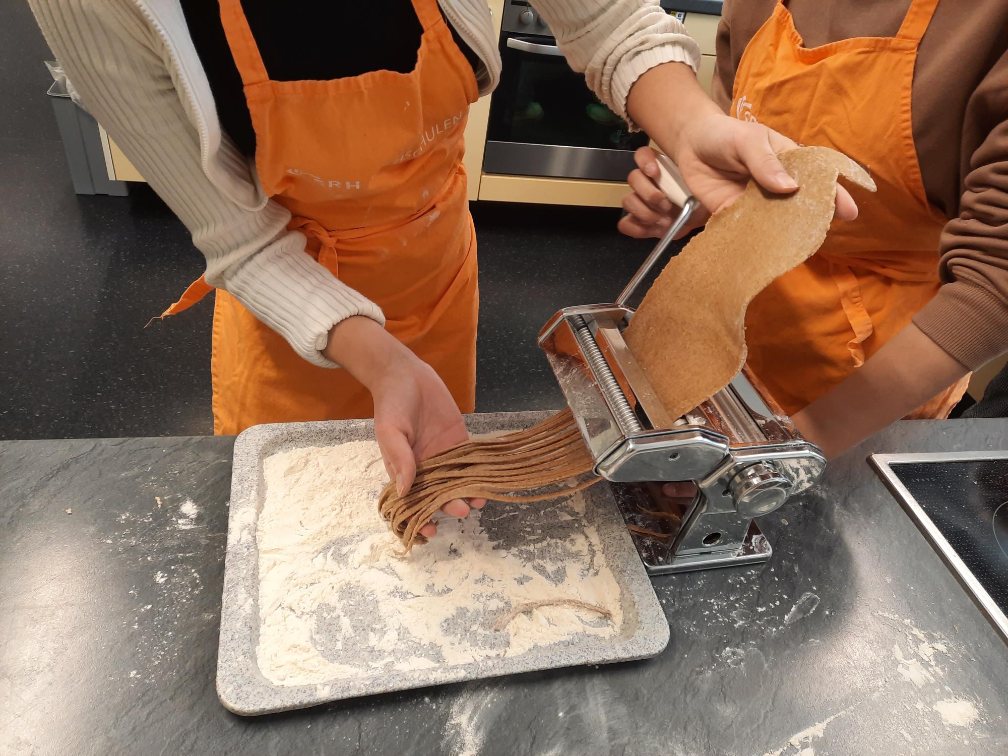 Drei Personen machen Nudeln mit einer Nudelmaschine.