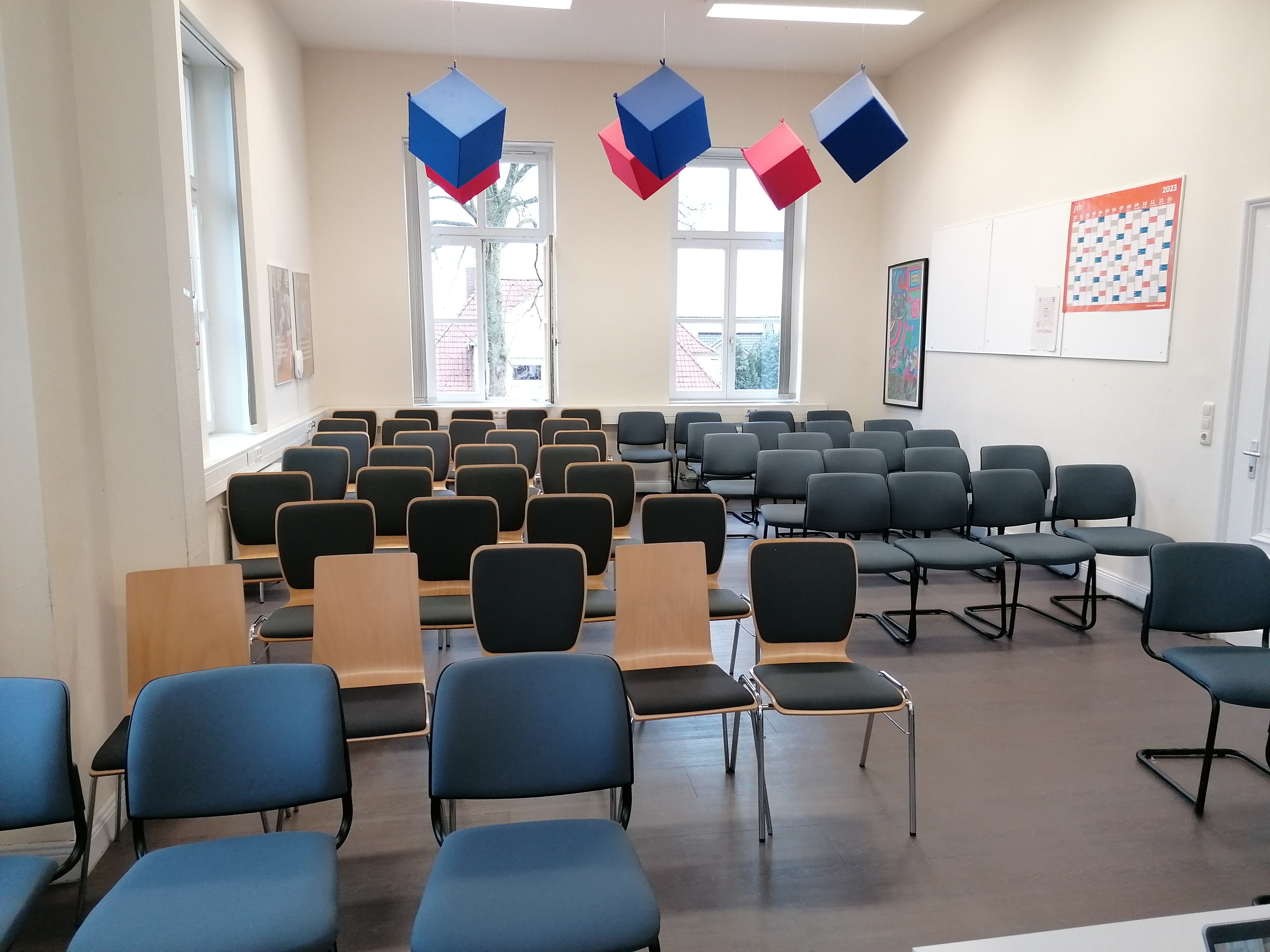 Ein leerer Raum mit Reihen von Stühlen und farbigen, hängenden kubischen Dekorationen.