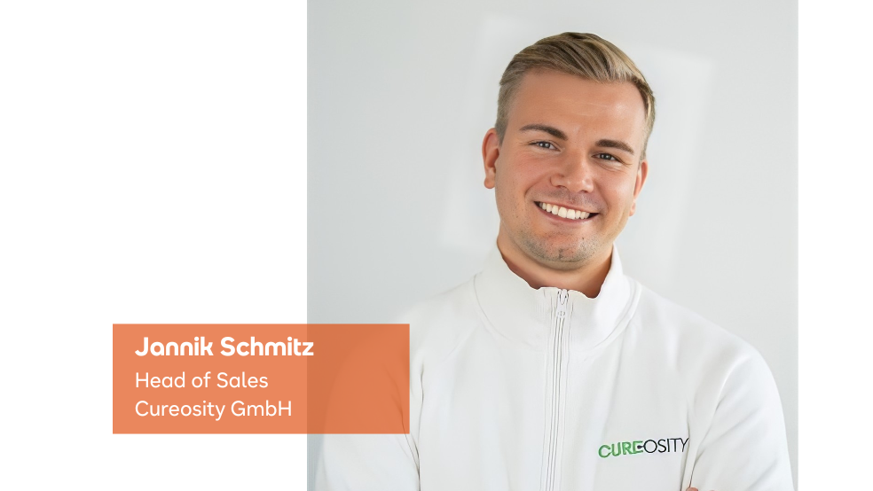 Ein professionelles Porträt von Jannik Schmitz, dem Head of Sales bei Cureosity GmbH, lächelnd vor einem weißen Hintergrund.