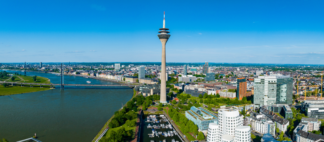Ein hoher Fernsehturm steht neben einem Fluss in einer Stadtlandschaft.
