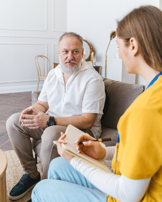 Aphasie-Behandlung: Logopädin sitzt mit einem Patienten zusammen und macht sich Notizen im Gespräch.
