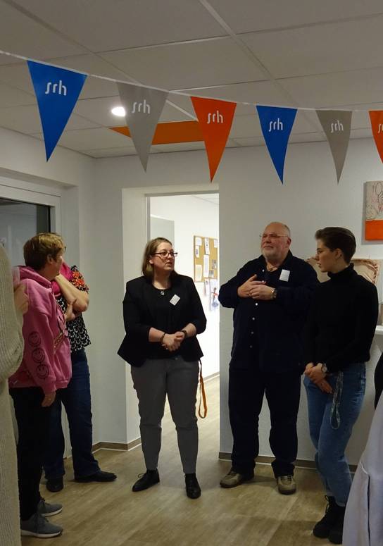 Eine Gruppe von Menschen steht in einem Raum mit bunten Bannerflaggen und betrachtet Kunstwerke.