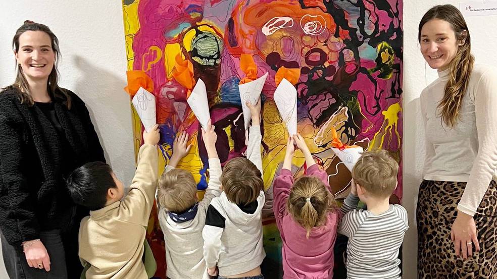 Eine Gruppe Erwachsener und Kinder posiert vor einem lebhaften Gemälde.