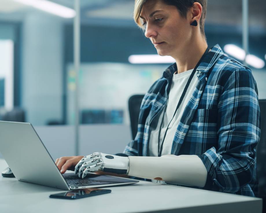 Frau tippt an ihrem Laptop und besitzt einen Robotik Arm