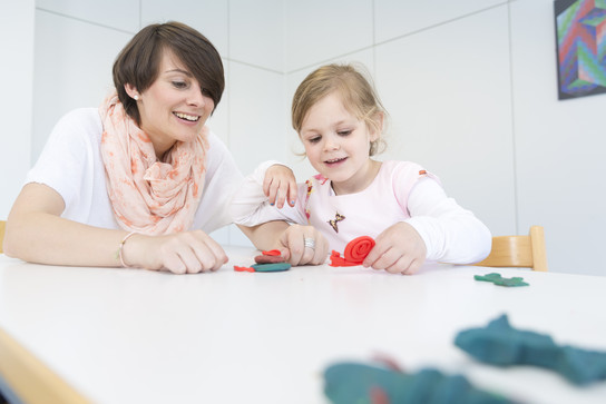 Eine Frau und ein kleines Mädchen spielen mit Knetmasse an einem Tisch.