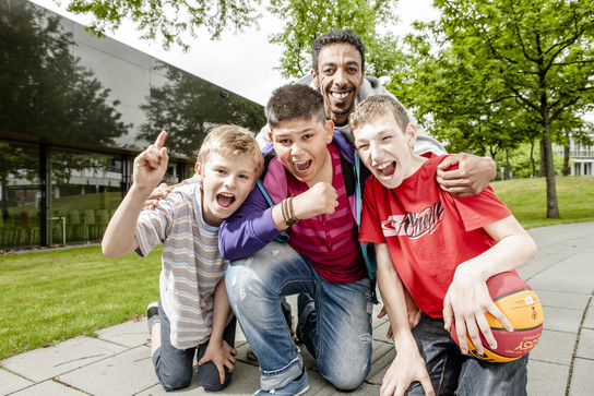 Ein Mann kniet mit drei Jungen zusammen, alle lachen und halten einen Basketball.