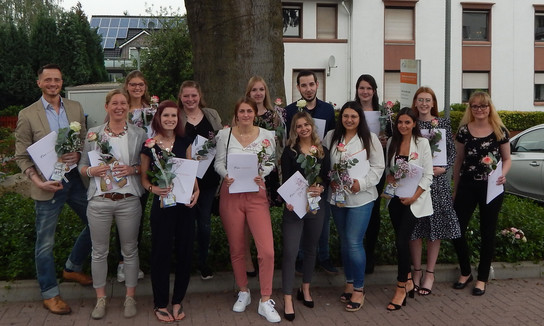 Eine Gruppe von Menschen posiert für ein Gruppenfoto, jeder hält einen Strauß Blumen und ein Zertifikat.