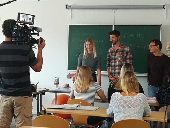 Ein Filmteam filmt eine Gruppe von Menschen in einem Klassenzimmer.