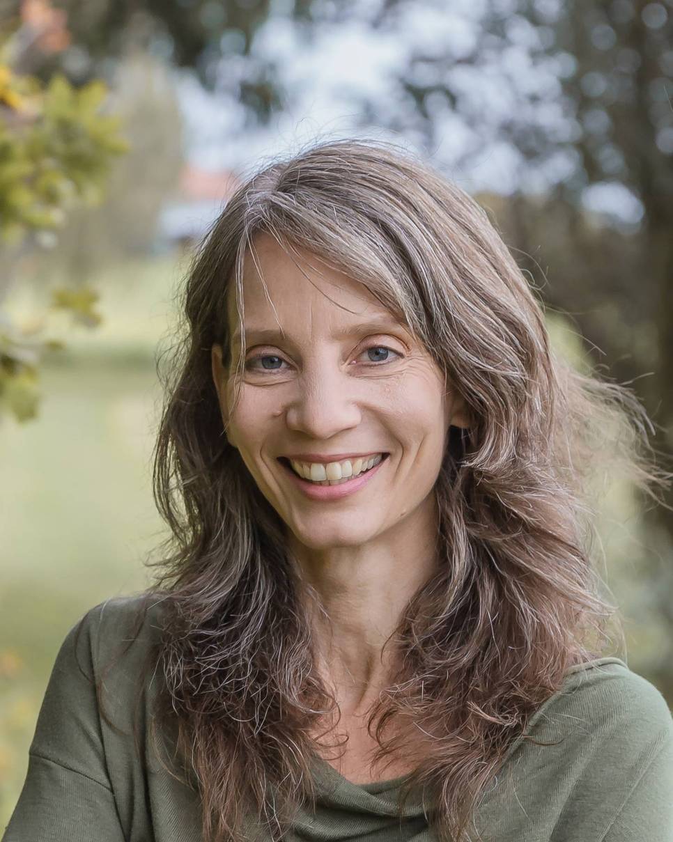 Ein Porträt einer Frau mit langem, lockigem Haar, die im Freien lächelt.