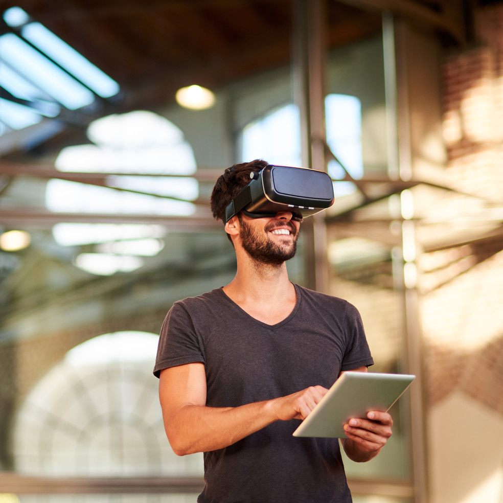 Mann steht im Freien, trägt eine VR Brille und hat ein Tablet in der Hand