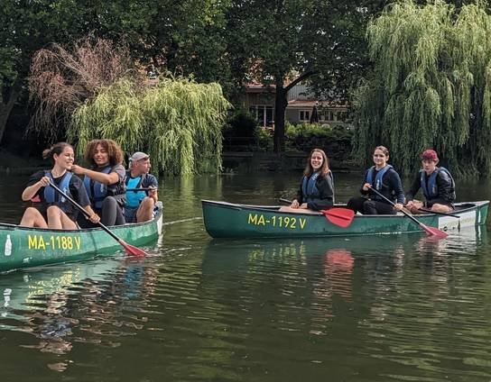 Eine Gruppe von Menschen paddelt in zwei Kanus auf einem Fluss.