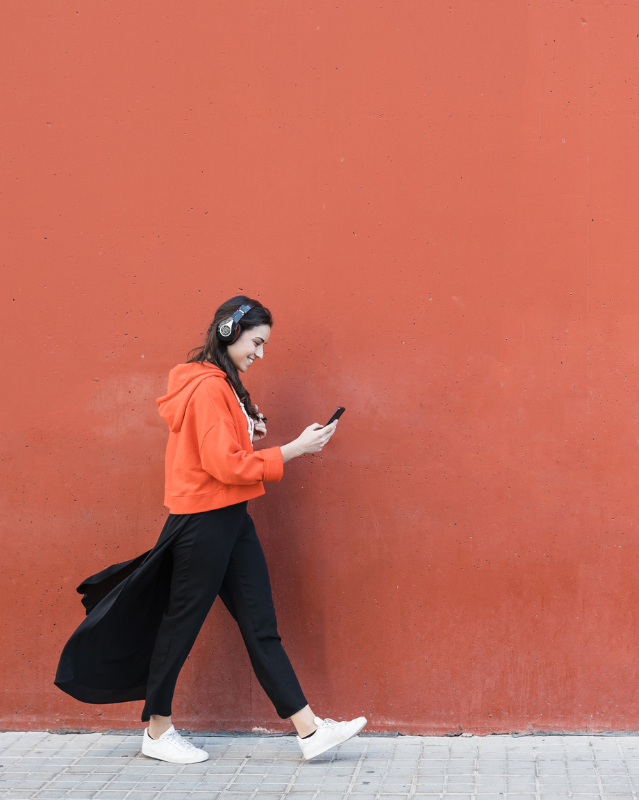 Mädchen läuft vor orangenem Hintergrund und schaut auf Handy