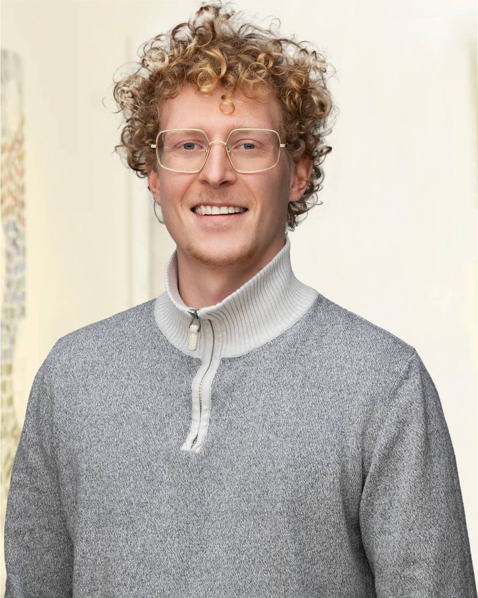 Ein Mann mit lockigem Haar und Brille lächelt in die Kamera.