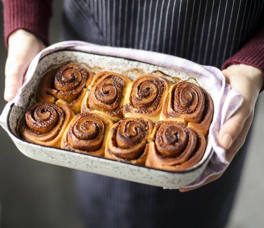 Person hält ein Backblech mit Zimtschnecken.