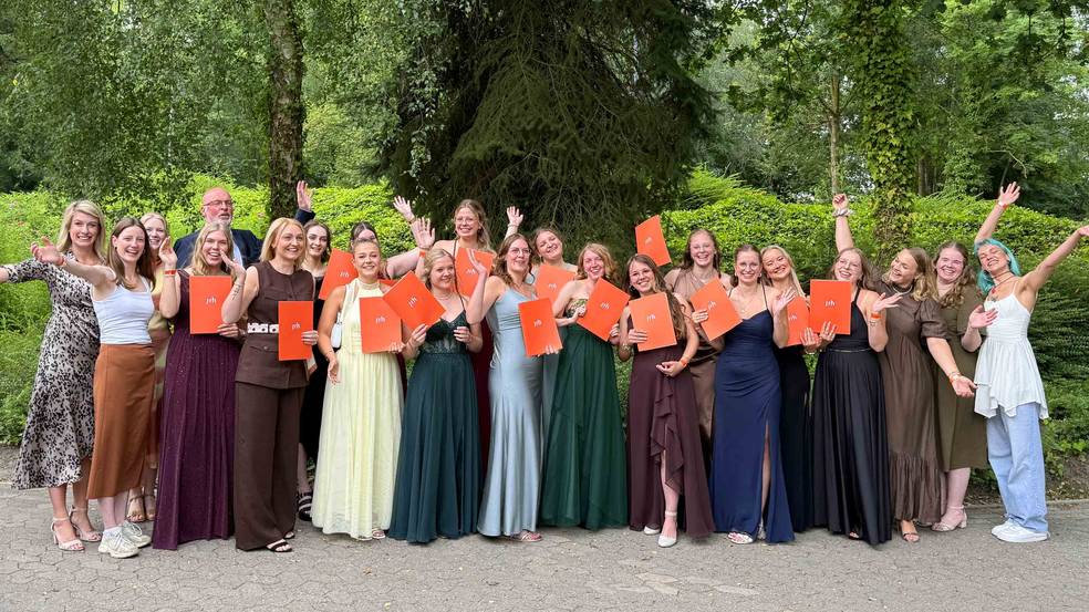 Abschlusskurs steht für ein Gruppenbild lächelnd zusammen und hebt ihre Hände
