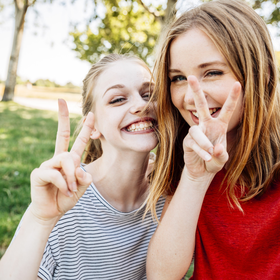 Zwei Mädchen machen ein Selfie und zeigen dabei das Peace Zeichen