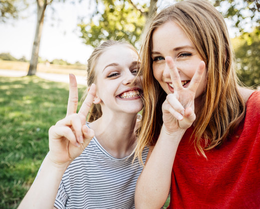 Zwei Mädchen machen ein Selfie und zeigen dabei das Peace Zeichen
