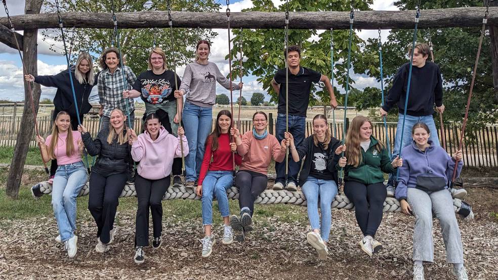 Eine Gruppe von angehenden Logopäd:innen schaukeln zusammen nebeneinander und lachen fröhlich in die Kamera