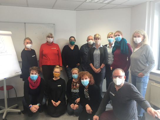 Gruppe von Menschen in einem Raum, alle tragen Masken und posieren für ein Foto.