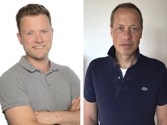 Zwei Männer in Poloshirts posieren nebeneinander vor einem weißen Hintergrund.