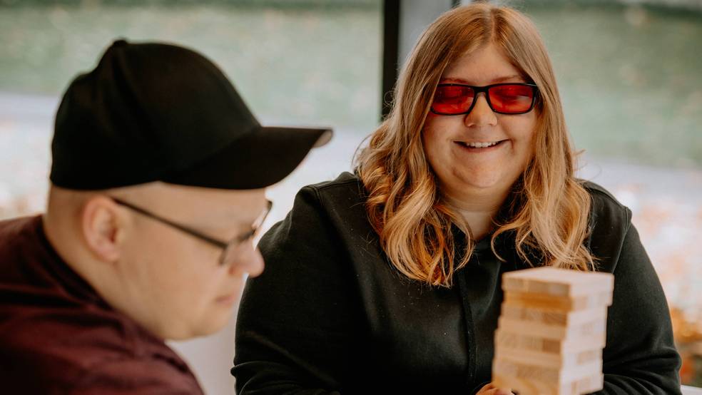 Eine Frau mit Sonnenbrille spielt Jenga mit einem Mann, der eine Baseballkappe trägt.