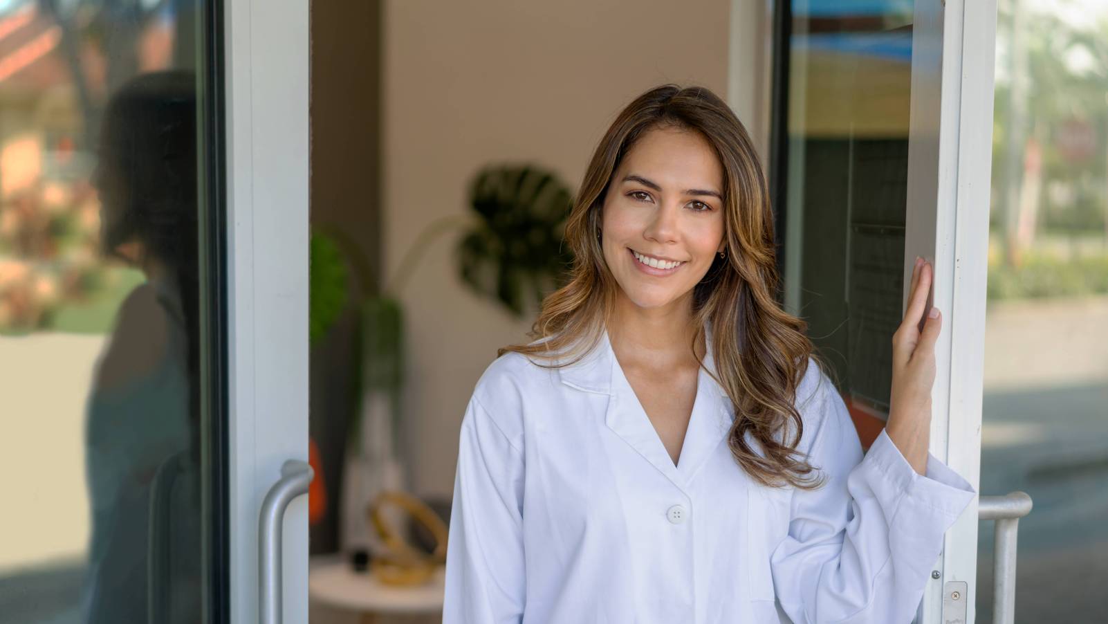 Ein Porträt einer lächelnden Ärztin, die die Tür ihrer Praxis öffnet und in die Kamera schaut.