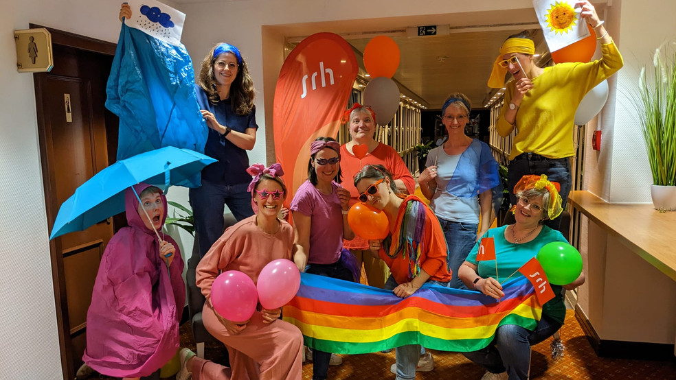 Eine Gruppe von Menschen feiert in farbenfrohen Kostümen und mit bunten Ballons.