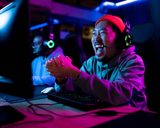 Ein Mann sitzt an einem Computer, lacht und trägt ein Headset.