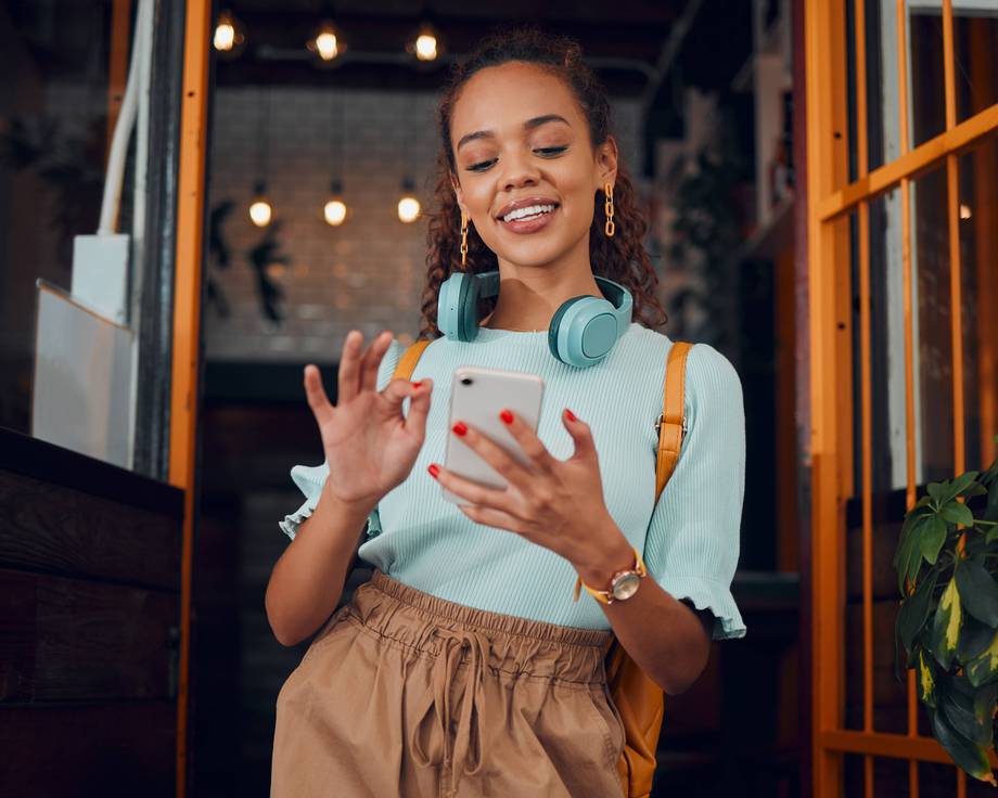 Eine junge Frau mit Kopfhörern hält ein Telefon und lächelt.