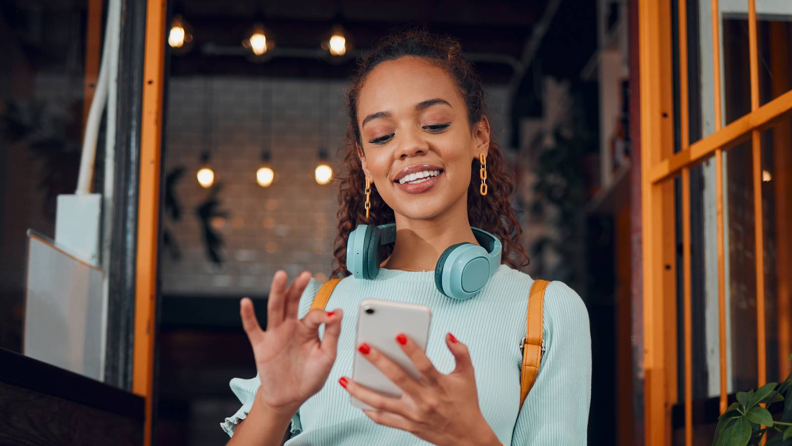 Eine junge Frau mit Kopfhörern hält ein Telefon und lächelt.