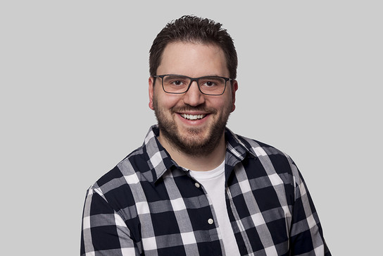 Ein Mann mit Brille und einem karierten Hemd lächelt.