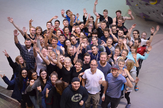 Große Gruppe von Menschen posiert für ein Gruppenfoto, alle lächeln und machen Handzeichen.