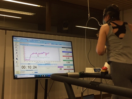 Frau trainiert auf einem Laufband vor einem Computerbildschirm mit Trainingsdaten.