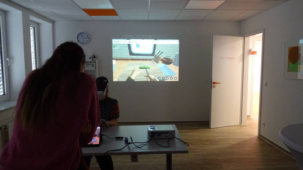 Zwei Personen sitzen an einem Tisch und spielen ein Videospiel auf einem Projektor.