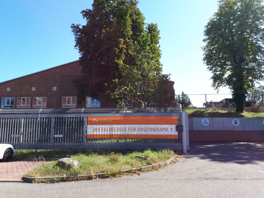 Ein Schild für die SRH Fachschule für Ergotherapie vor einem Ziegelgebäude.