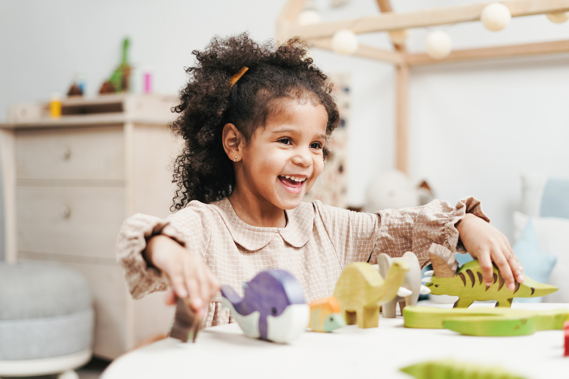 Lachendes Mädchen spielt mit Holztier-Spielfiguren an einem Kindertisch