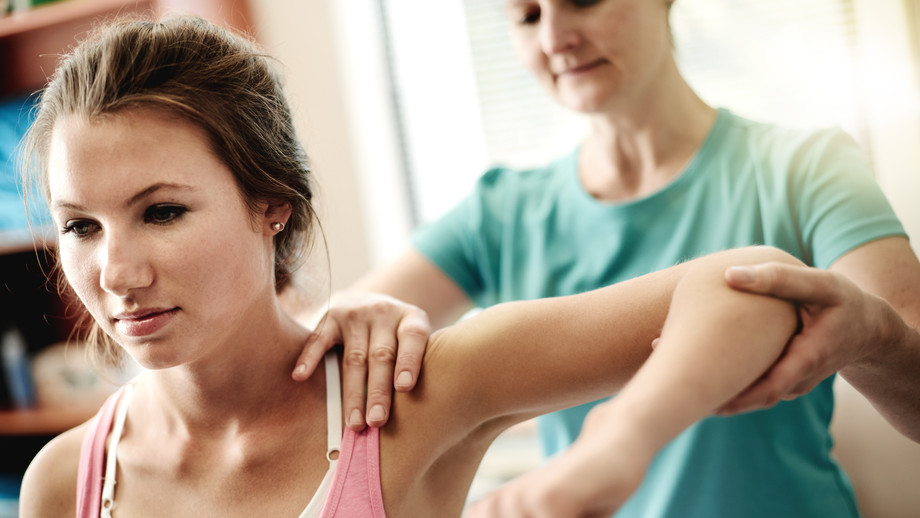 Junge Frau wird von Physiotherapeutin an der Schulter behandelt