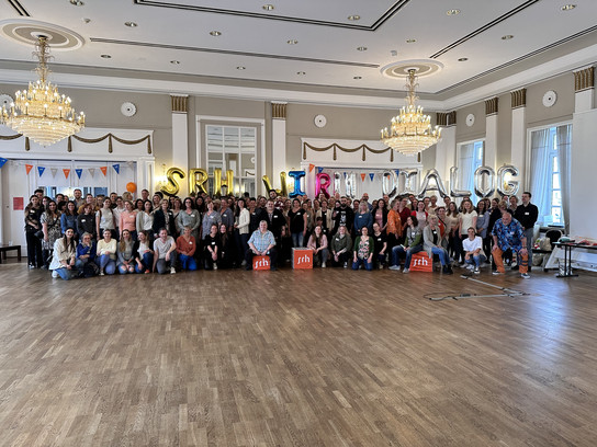 Große Gruppe von Menschen posiert für ein Gruppenfoto in einem Ballsaal.