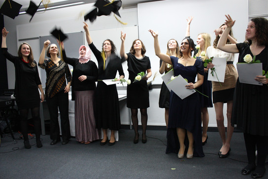 Eine Gruppe von frischgebackenen Absolventinnen feiert, wirft ihre Hüte in die Luft und hält Blumen und Diplome.